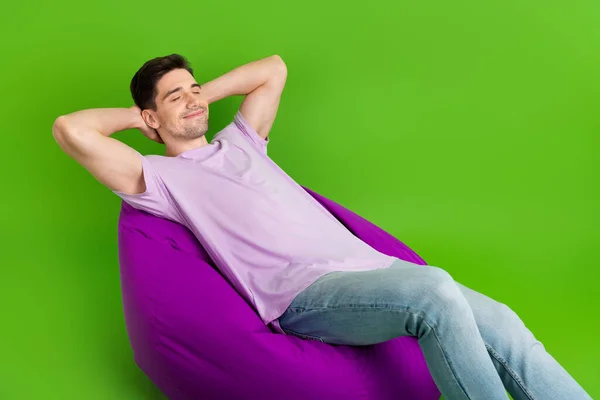 Full length photo of satisfied man closed eyes wear trendy clothes hold hands behind head empty space isolated on green color background.