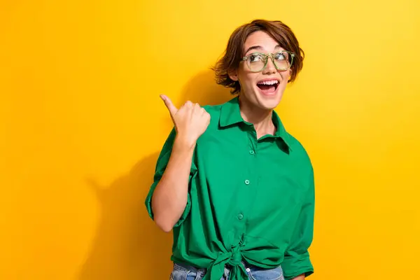 Photo of impressed excited lady wear green shirt spectacles looking showing thumb empty space isolated yellow color background.
