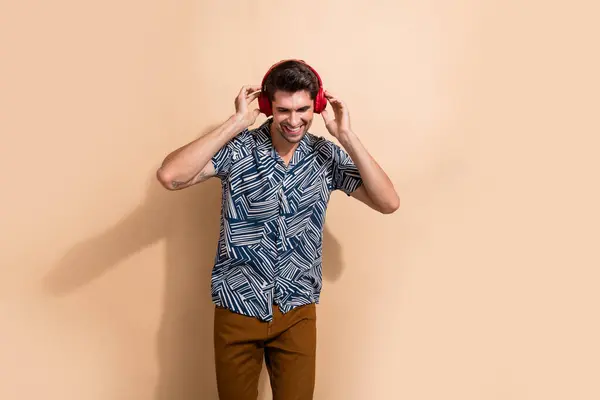 ポジティブクールな男の写真 トレンディな衣装ハンドホールドワイヤレスイヤホンリスニングMp3プレーヤーベージュ色の背景に隔離 — ストック写真