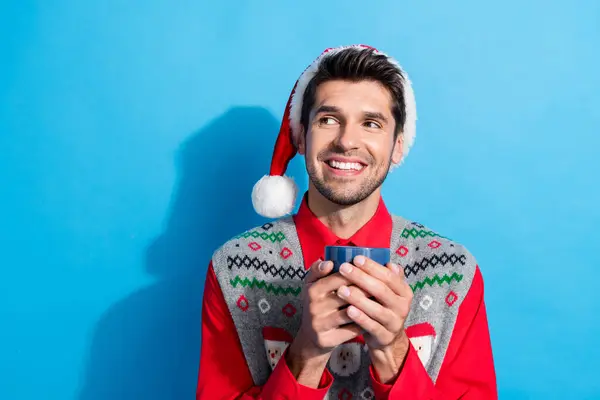 楽観的な陽気な夢見る男の写真は クリスマスの帽子を着用しています 空のスペースは 青い色の背景で隔離された手でカカオのカップを保持します — ストック写真