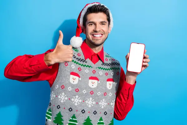面白い男の写真は 青い色の背景に隔離されたスマートフォンディスプレイ上のアプリを推奨クリスマスの帽子を着用します — ストック写真