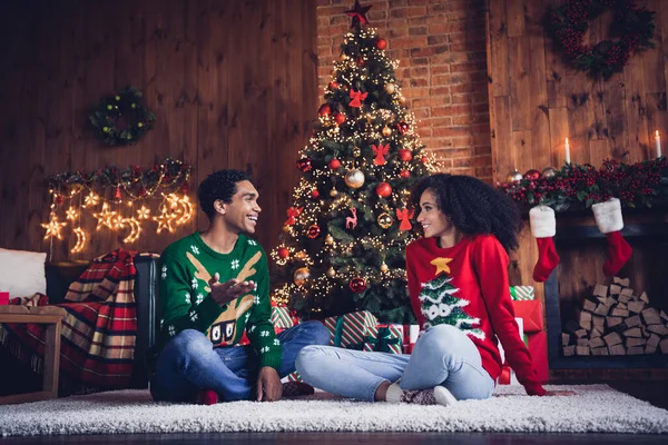 Full body portrait of two peaceful cheerful people sit comfy carpet floor chatting enjoy fairy christmastime apartment indoors.
