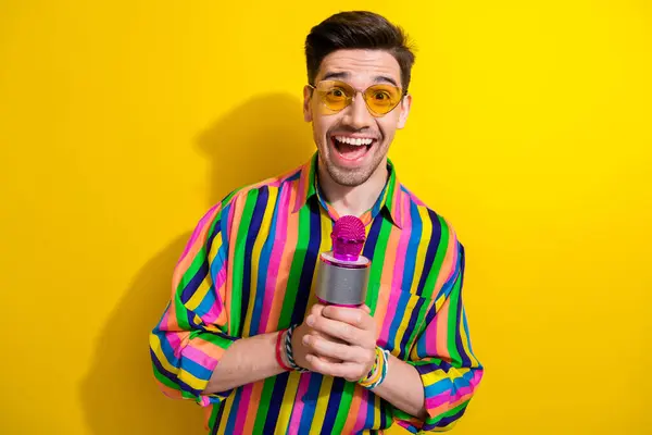 Photo of happy hipster man holding microphone when his turn to make a toast at nostalgia style party isolated on yellow color background.