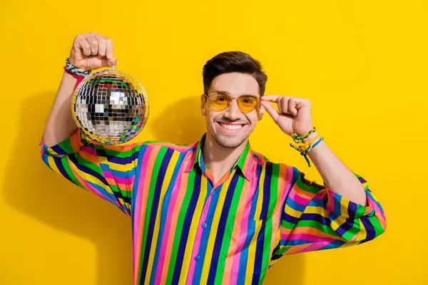 ヒップスターハンサムな男の写真ストライプカラフルなシャツタッチサングラスは 黄色の背景に隔離されたパーティーでディスコボールを掛けています — ストック写真