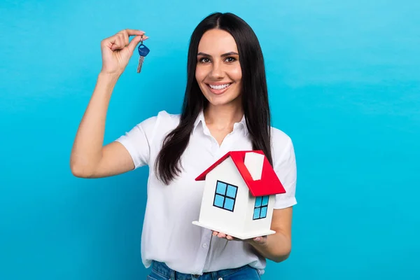 Photo of sweet shiny lady wear white shirt rising keys holding little red roof house isolated blue color background.