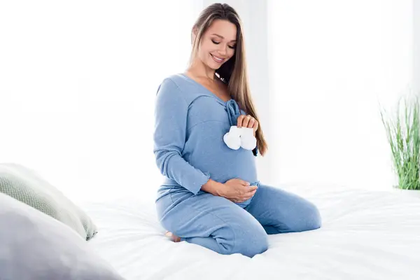 美しい甘い優しい母親の写真 屋内で寝室の白いライトに座っている新生児のための服を準備する — ストック写真