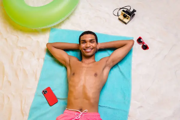 Photo of positive pretty masculine guy lying towel arms behind man tanning outdoors seaside beach.