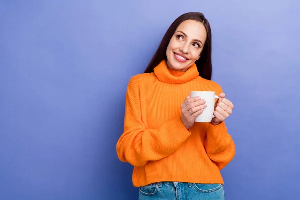 Photo of smiling woman wear orange sweater hold cup hot tea coffee break look new tv show empty space isolated on purple color background.