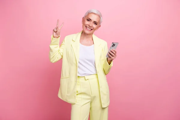 友好女性商业影响者形象展示V标志手持手机 用于共享粉色背景下隔离的内容 — 图库照片