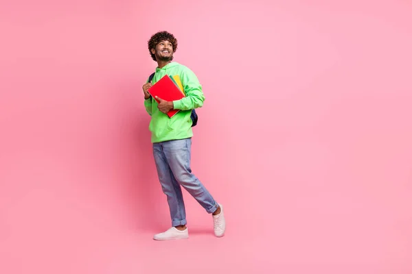 Full body length photo of young cheerful man student bring notebooks looking empty space dreaming isolated on pink color background.