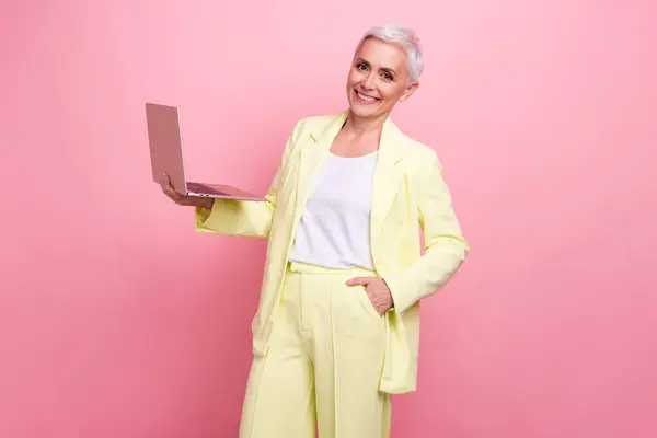 Photo confident ceo boss woman in yellow suit holding laptop using social networks to hunt new employees isolated on pink color background.