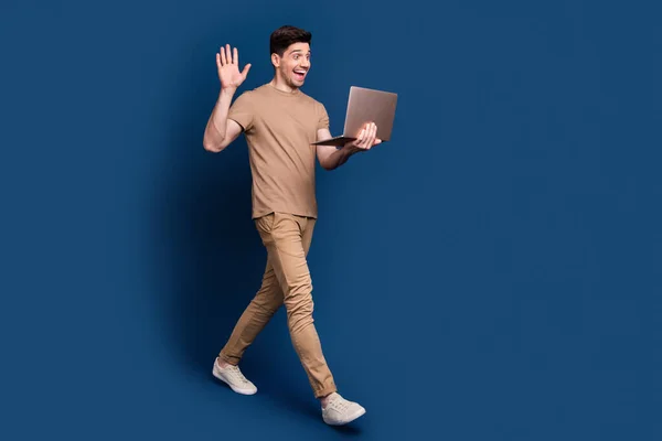 Full length photo of cheerful man wear beige stylish outfit waving palm say hi at laptop on webcam isolated on dark blue background.
