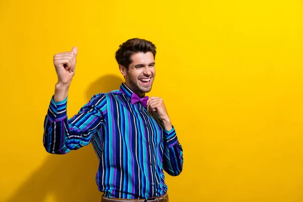 Photo of ecstatic positive man with bristle dressed striped shirt touch bow tie dancing at party isolated on vivid yellow color background.