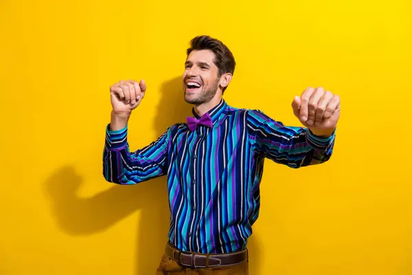 照片上的好心情英俊的男人 身穿条纹衬衫 头戴蝴蝶结领带 在鲜亮的黄色背景下跳舞 显得很开心 — 图库照片