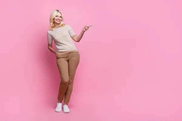 Full size photo of satisfied person dressed striped t-shirt pants indicating at proposition empty space isolated on pink color background.