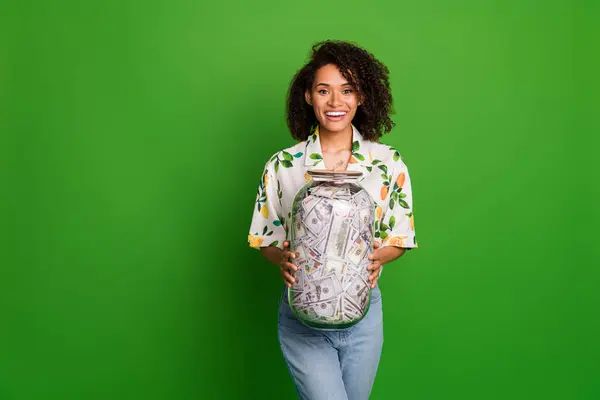 Photo of excited funky lady wear print shirt holding money jar empty space isolated green color background.