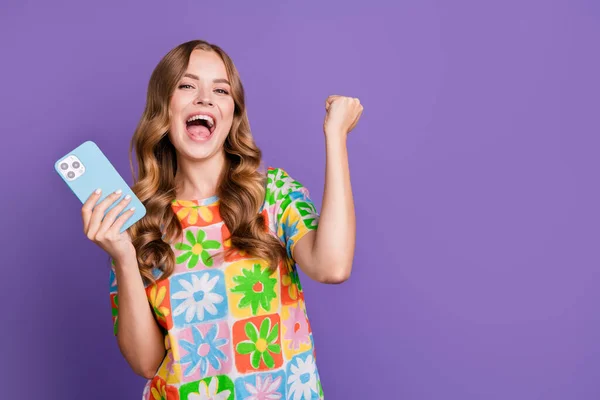 Photo of overjoyed ecstatic woman with wavy hairstyle holding smartphone screaming yeah win bet isolated on purple color background.