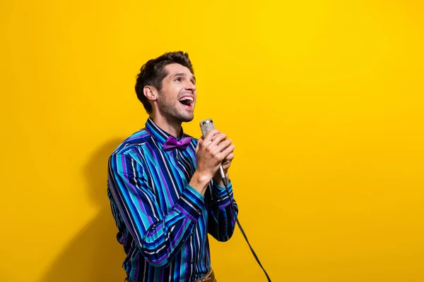 时尚男子穿着条纹衬衫蝴蝶结唱着歌曲在麦克风中寻找空旷的空间隔离在黄色背景下 — 图库照片