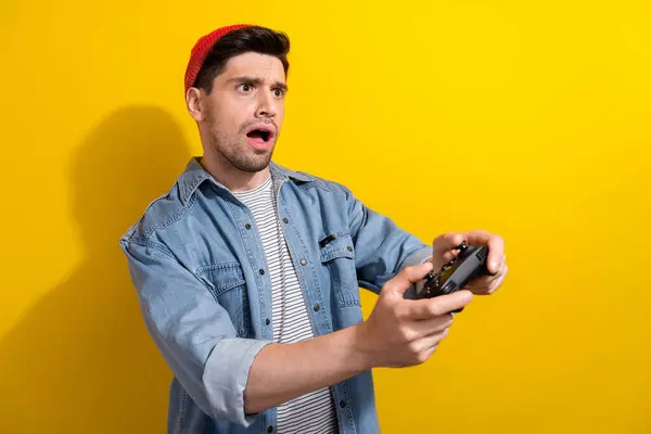 衝撃を受けた男性の写真は プレイステーションゲームを緩めるデニムジャケットを着用しています 空のスペース 隔離された黄色の背景 — ストック写真