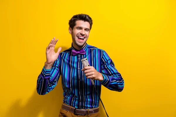 照片上 穿着条纹衬衫的心情不错的男人打着蝴蝶结领带拿着话筒站在舞台上笑 背景是鲜亮的黄色 — 图库照片