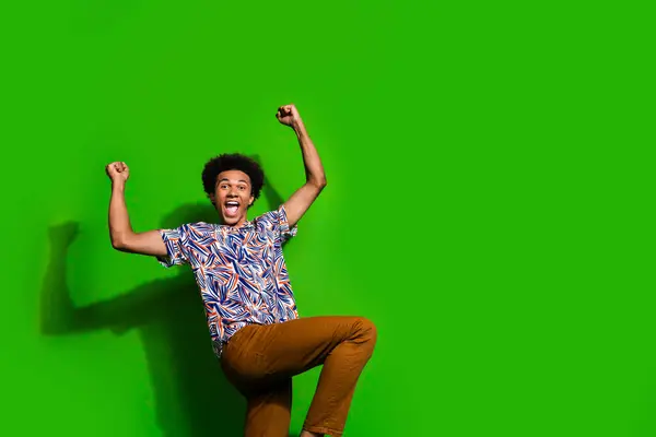 Photo of lucky excited man dressed print shirt rising fists shouting yeah empty space isolated green color background.