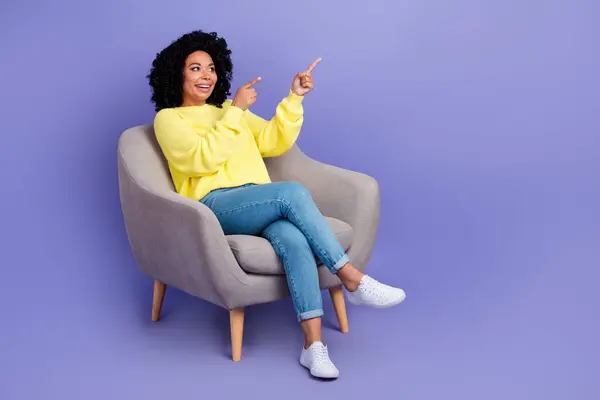 Full body photo of funny person wear knit pullover sit in armchair look at sale directing empty space isolated on purple color background.