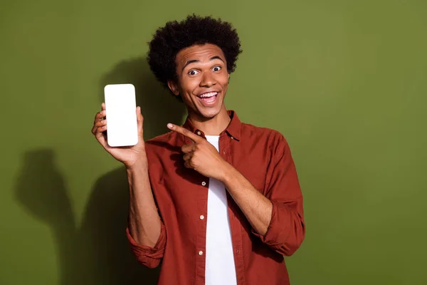 Photo of ecstatic man in shirt indicating at impressive ui design empty space on smartphone display isolated on khaki color background.