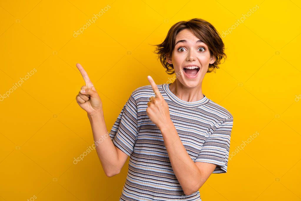 Portrait of crazy girl with short hair wear grey t-shirt directing at impressive offer empty space isolated on yellow color background.