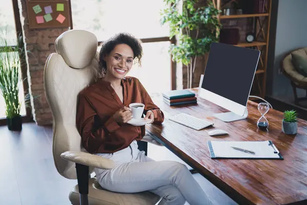 Photo of stunning positive company founder lady sitting chair hold aroma coffee cup workstation business center inside.