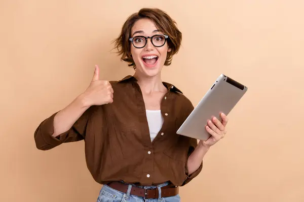 Photo of confident excited lady wear brown shirt spectacles thumb up working apple samsung modern device isolated beige color background.