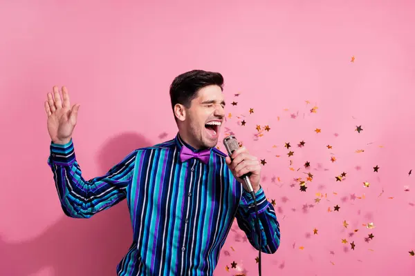 Photo of excited overjoyed person hold microphone sing flying stars confetti isolated on pink color background.