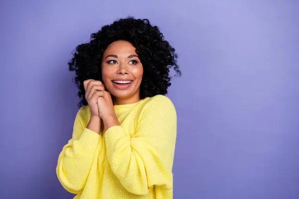 Photo of kind woman with afro hair dressed yellow sweater hands near cheeks look at offer empty space isolated on violet color background.