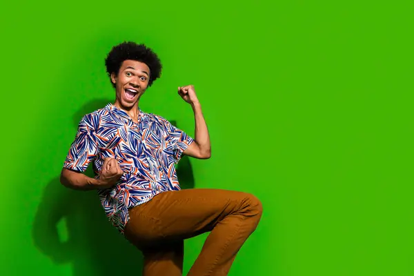 Photo of impressed lucky man dressed print shirt rising fists yelling yeah empty space isolated green color background.