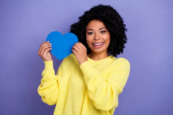 Portrait of cheerful kind person with chevelure wear knit pullover hold big blue heart near face isolated on purple color background.