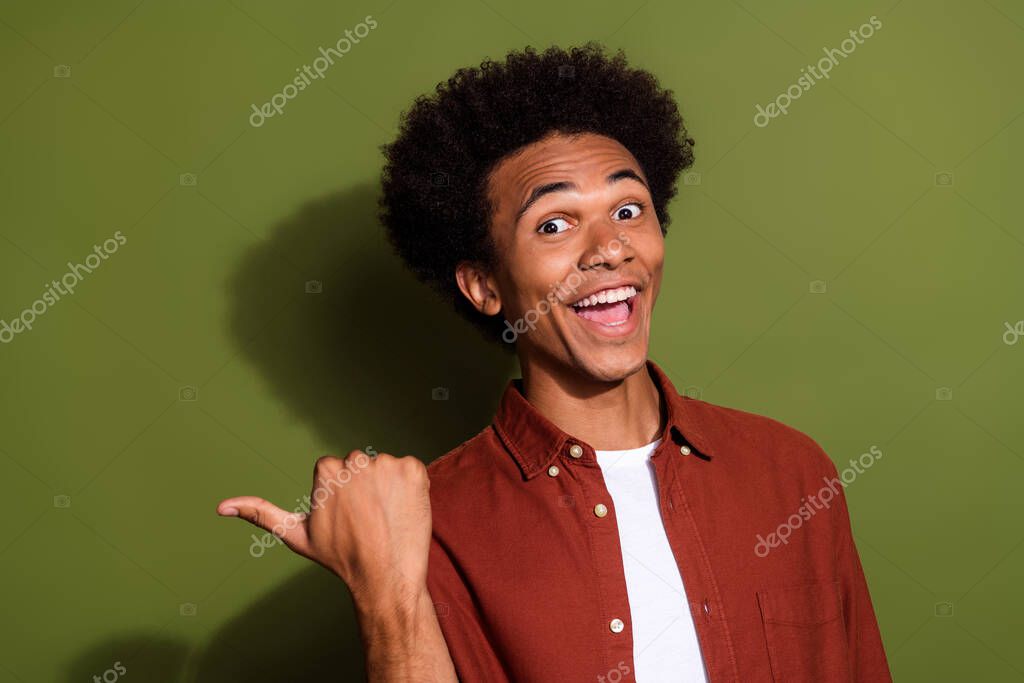 Portrait of astonished guy with chevelure wear stylish shirt indicating at discount empty space isolated on green color background.
