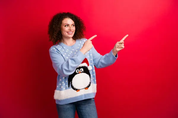 Photo of interested in ugly sweaters store pointing fingers empty space advertisement winter shop isolated on red color background.