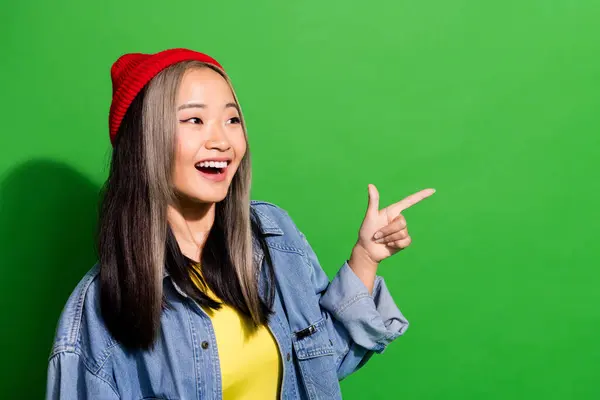 Photo of positive excited lady wear denim jacket looking pointing finger empty space isolated green color background.