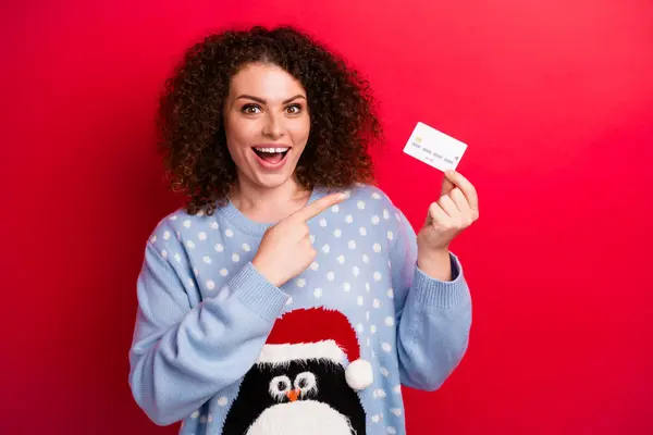 驚いた若いカーリーレディポイントフィンガー決済カードの写真赤い色の背景に隔離されたキャッシュバックでクリスマスショッピングをお勧めします — ストック写真