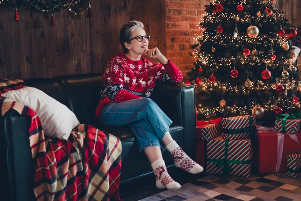 Full size photo of peaceful minded grandmother sitting comfy sofa brainstorming enjoy evergreen tree lights house indoors.