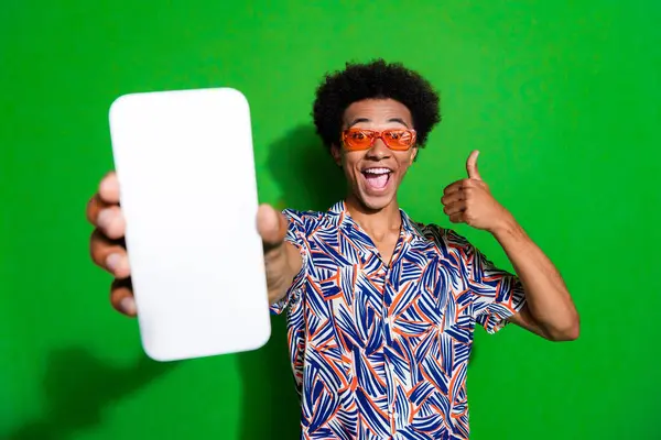 Photo of excited confident man dressed print shirt eyewear showing thumb up modern gadget empty space isolated green color background.