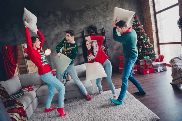 Full body portrait of group positive buddies have good mood pillow fight living room decorated flat inside.