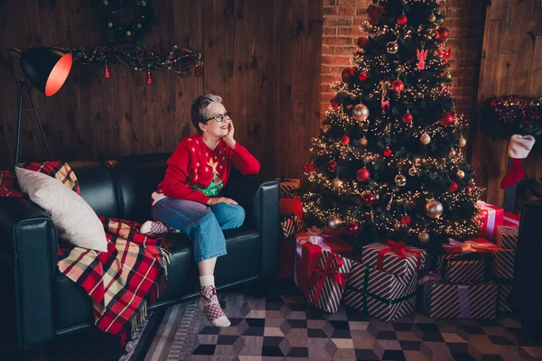 Full body length photo of beautiful harmony atmosphere mature aged woman white hair grandmother sitting couch touch cheek enjoy xmas vibes.