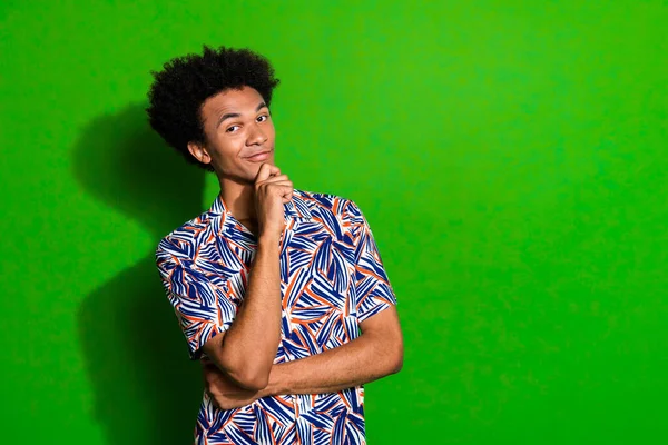 Portrait of confident guy student touch chin with serious face expression wearing tropical print shirt isolated on green color background.