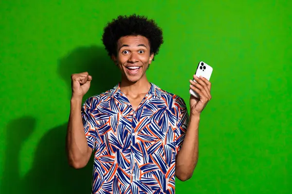 Photo of excited lucky man dressed print shirt winning game modern gadget isolated green color background.