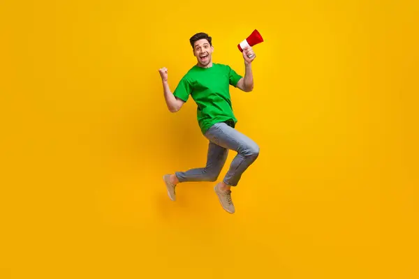 Full length photo of satisfied ecstatic man jumping holding loudspeaker shout yeah win lottery isolated on yellow color background.