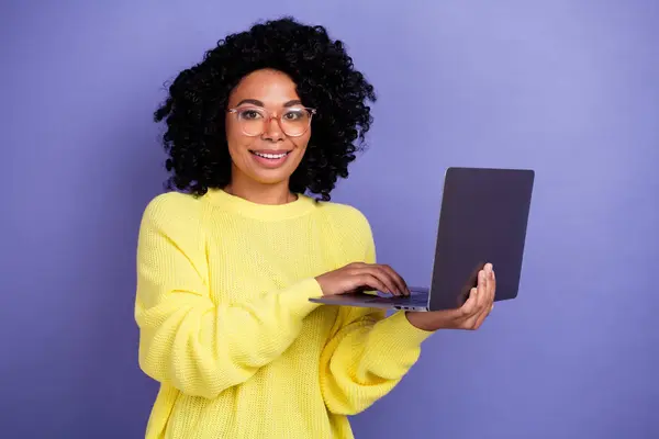Photo of smart woman with afro hairstyle dressed yellow sweater in eyewear hold laptop write email isolated on violet color background.