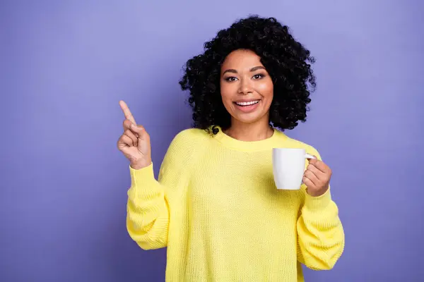 Portrait of pleasant funny person wear knit pullover hold mug directing at coffee shop empty space isolated on purple color background.
