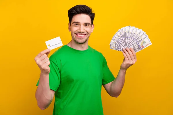 stock image Photo portrait of attractive young brunet man hold money fan credit card dressed stylish green clothes isolated on yellow color background.