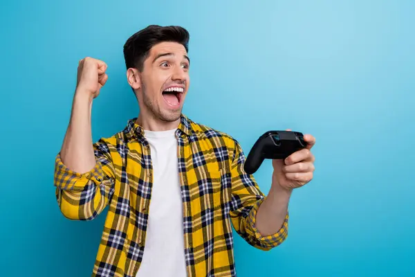 Photo of excited lucky man dressed yellow plaid shirt winning playstation video game empty space isolated blue color background.
