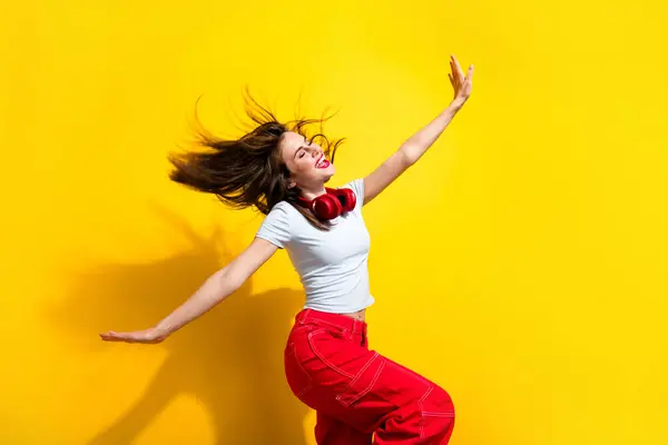 Photo of excited sweet woman dressed white t-shirt headphones flying hair dancing discotheque arms sides isolated yellow color background.